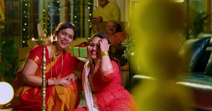 Lighting traditional samai with diya, Indian young girl in ethnic wear and senior mother joyfully celebrating Hindu festival Diwali in evening at home with festive decor and glowing diya illumination