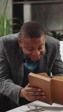 African-American man tutor laughs reading task in textbook with junior boy student at private English language lesson with native speaker slow motion