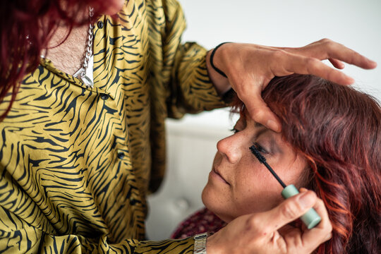 Non-binary makeup artist applying mascara on friend celebrating body positivity