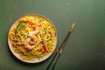 Delicious pad thai noodles with shrimp, peanuts, lime, red bell pepper, and green onion on a textured green background with chopsticks top view, copy space