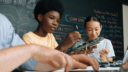Young student fixing controller while teacher programing engineering code at STEM class. Closeup of...