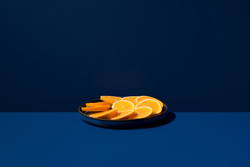 Fresh orange slices on a black plate with blue backdrop