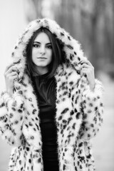 Portrait of a young beautiful girl in a winter faux fur coat in a city park. Black and white photo.