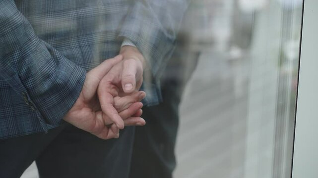 Man in business suit nervously rubs and fidgets fingers from behind closeup. Nervous and tense atmosphere and involuntary movements of person behind glass wall in office during deal negotiations.