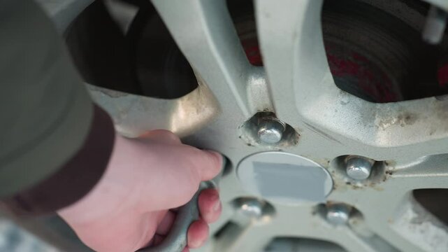Close up of mechanic hand using spanner to loosen wheel bolt on car rim, with blurred snowy background, metal details and manual work clearly visible