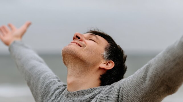 Man with arms outstretched eyes closed in open expression gray day by the sea serenity and peace