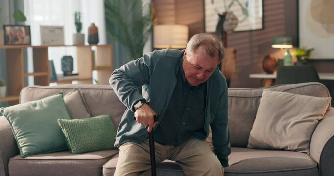 Senior man, walking stick and sofa in home with back pain, steps and recovery from injury in retirement. Elderly person with disability, cane and rehabilitation for spine in living room at house