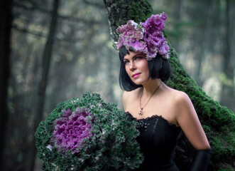Portrait of a young brunette woman in a creative image. A large head of decorative cabbage and a hat made of cabbage leaves. Art photography.