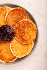Freshly cooked fluffy pancakes are arranged neatly on a circular beige plate, accompanied by a small bowl of delicious berry jam, ideal for breakfast or brunch.