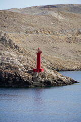 Vertical photo of a small lighthouse on a rocky island in the azure blue sea