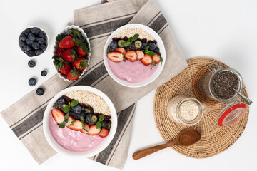Presented by fruits putting yogurt toppings with strawberry, berry, oats, raisins and chia seed decorated by peppermint in white blow. Pink background. Set of healthy dairy product choice. Pecuniary.