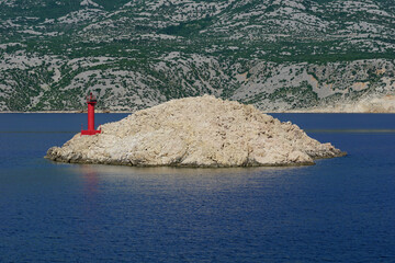 Lighthouse on a rocky island surrounded by azure blue sea in front of the mainland