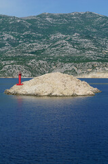 A small rocky island with a red lighthouse in front of the mainland