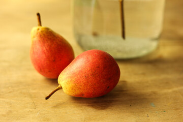 Red pears on a wooden table with a glass vase in the background.