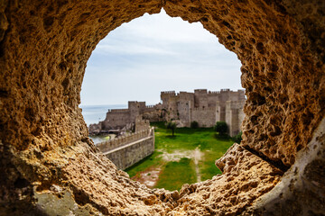 Magnificent Ancient Stone Castle Framed Through a Rocky Circular Opening Under Blue Sky..