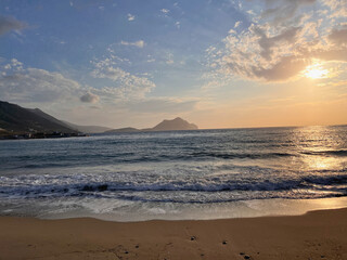 Sunset over the Aegean Sea from Aegiali beach on Amorgos island, Greece, with soft waves, golden sky, mountainous horizon, and tranquil coastal landscape