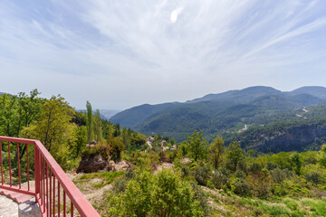 Elevated garden area with greenery, a red rail fence, and stunning views of distant blue mountains under a bright clear sky...