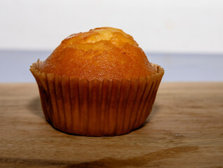 A freshly baked muffin sits on a wooden surface, presenting a golden brown top. The warm lighting highlights its texture, inviting those who see it to enjoy a tasty treat with coffee or tea