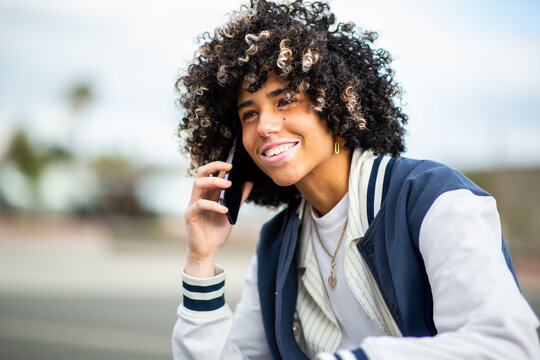 Smiling young woman with curly hair and skin condition talking on phone in casual jacket