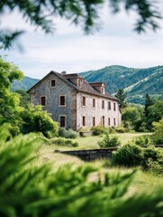 Obraz premium Stone House in Mountain Valley - A rustic stone house sits serenely in a lush green valley, mountains forming a picturesque backdrop