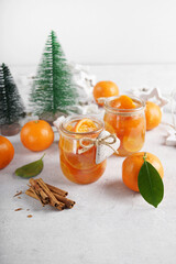 Homemade tangerines jam with orange peel in a glass jar as a gift for Christmas or New year with fir branches, spices (cinnamon and anise). Selective focus.