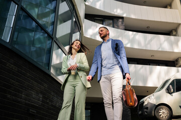 Two happy business people, a man and a woman, walking and chatting outside their office, enjoying...