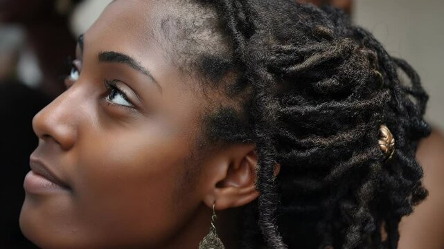 Close-up portrait of a contemplative woman with natural black dreadlocks, wearing earrings and gazing upwards in a serene and peaceful manner.