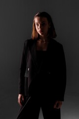 Confident individual dressed in black attire poses against dark backdrop in an artistic setting