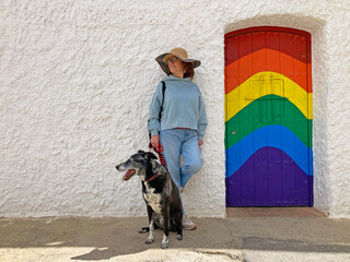 mujer modelo  con sombrero y perro posando en una calle con pared blanca al lado de una puerta pintada con los colores LGTB almería sur mediterráneo IMG_0951-as25