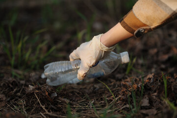 Close-up of a gloved hand lifting a discarded plastic bottle from the ground during an outdoor...