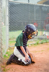 Young boy reluctantly playing the position of a baseball catcher