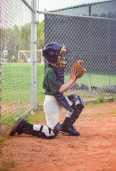 Young boy reluctantly playing the position of a baseball catcher