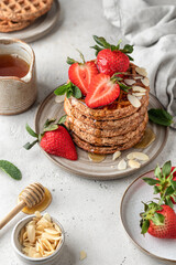 Oatmeal belgian waffles with strawberry, honey and almond petals stacked on a plate, white background