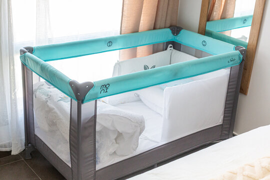 Modern portable crib with a turquoise mesh design, placed beside a cozy bed in a well-lit nursery, showcasing a safe sleeping environment for infants and toddlers