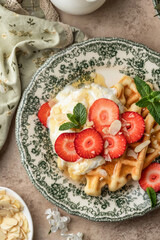 Homemade belgian waffles with strawberries, whipped cream and honey close up. Served on a rustic plate with spring flowers, top view