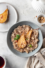 Wholegrain oatmeal porridge with caramelized pear, nuts and honey on white table with tea, healthy...