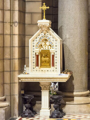 Principality of Monaco, France - July 9, 2024: Cathedral of Our Immaculate Lady. Small gold and white Shrine of sacrificial lamb with golden cross on top, closeup