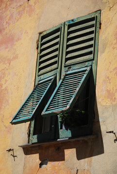 Fototapeta old window with green wooden shutters in tuscany style on yellow orange wall on sunny day with shadow