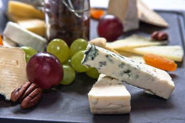 Cheese board. Assortment of cheeses with nuts, bread, grapes, fruit in syrup on stone slate plate. White background