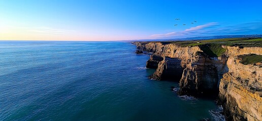 Dramatic coastal cliffs meet the turquoise sea under a pastel sky