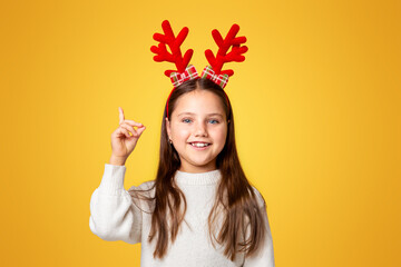 Great idea. Cheerful girl in horns and sweater shows thumb up to free space, isolated on yellow...