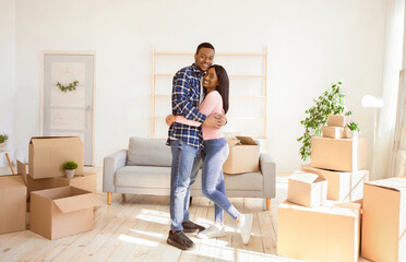 Romantic black newlywed couple hugging among cardboard boxes in their new apartment on relocation...