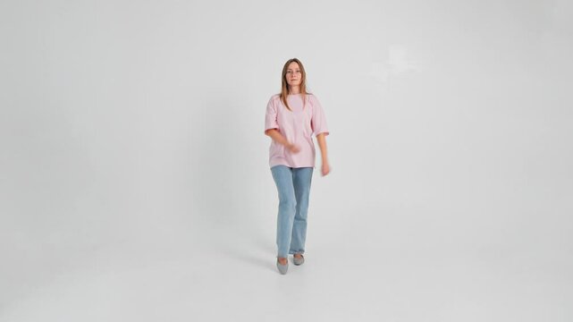 Woman is walking forward raising high knees like a soldier looking at camera then turning back. Isolated slow motion of Caucasian lady in casual clothes marching on white background. Parade theme