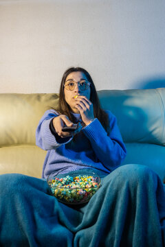 Young woman watching tv and eating popcorn on sofa at night