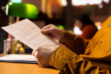 Public library scene with senior person studying under soft lighting, surrounded by books and paperwork, representing dedication to lifelong learning and the journey toward a university degree.