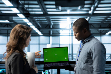 Employees in data center automating routine maintenance tasks with green screen laptop, executing...