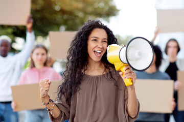 Multiracial young protestors striking on the street, holding megaphone and blank placards....