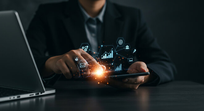 Person using a smartphone with digital icons and a laptop on a dark desk in a business setting real estate business ,technology ,selling ,purchasing ,agreement - Powered by Adobe