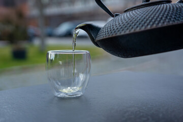 Pouring green tea into a glass from a metal kettle on blurred background, hot drink in teapot