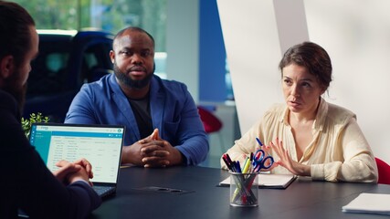 Customers in showroom completing credit application after being sold car insurance by salesman....
